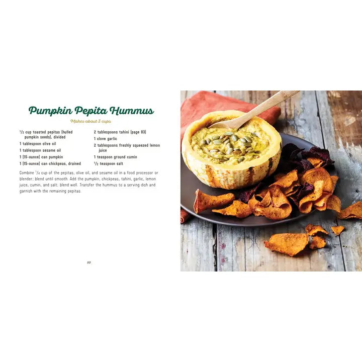 A recipe page from a cookbook showing the text for Pumpkin Pepita Hummus on the left and a prepared food photo on the right. The photo shows a baked hummus dip in a bowl with a wooden spoon, accompanied by pumpkin chips on a plate and scattered chips on a rustic wooden surface.
