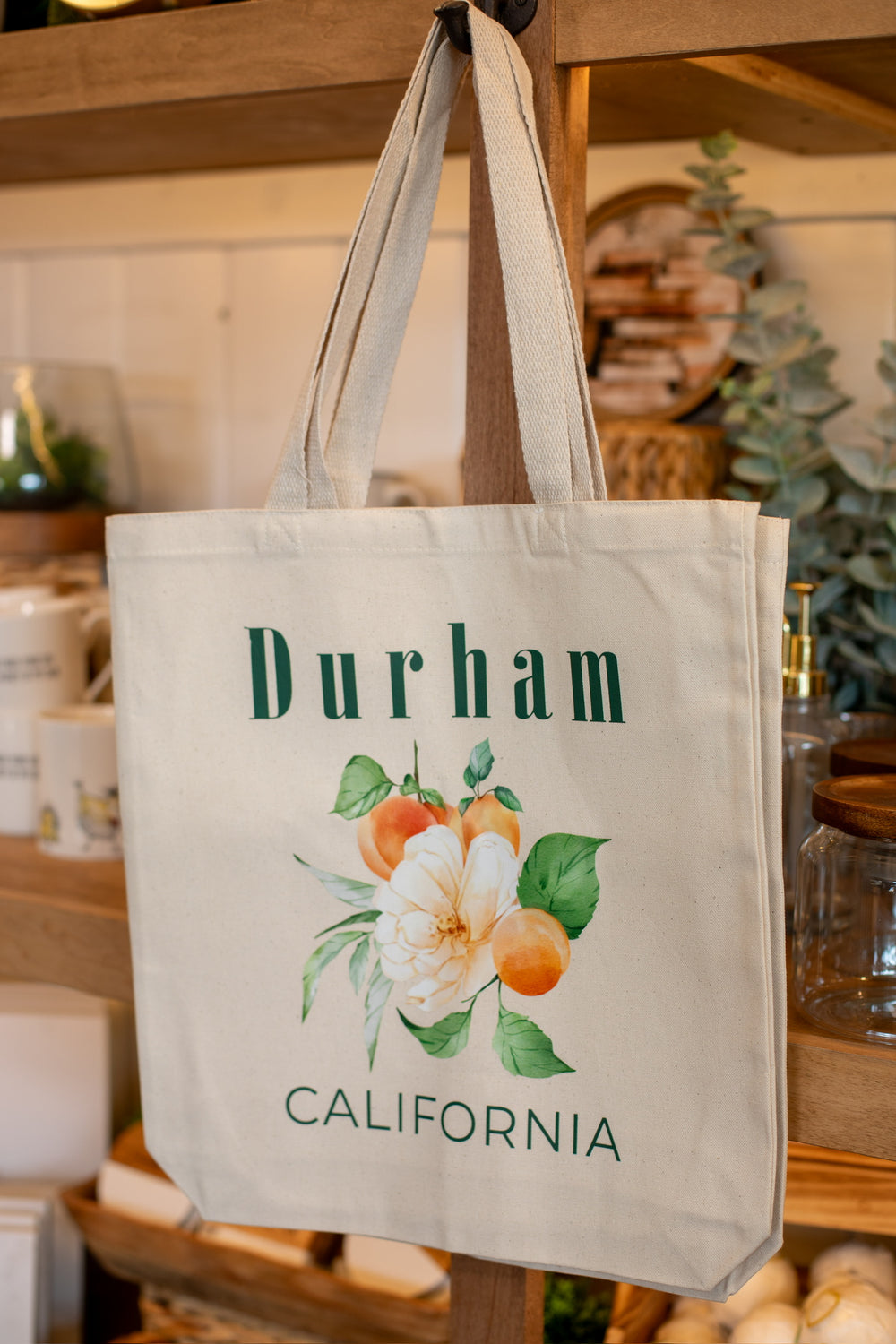 Beige tote bag with floral design and 'Durham California' text on a wooden surface.