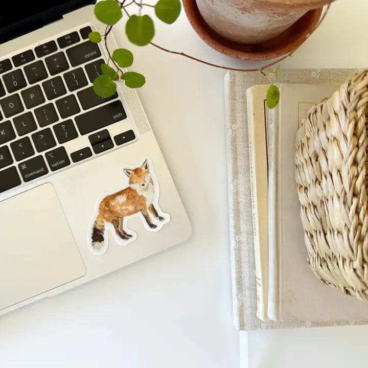Laptop with a fox sticker on a desk with a plant and book