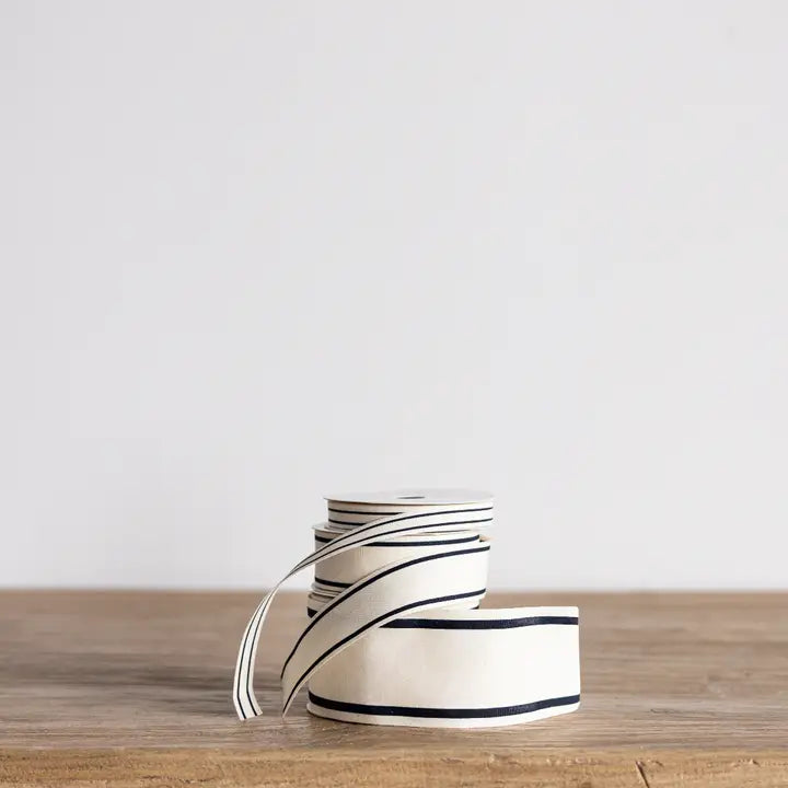 Cream and black edged ribbon in multiple widths displayed with other ribbon spools.
