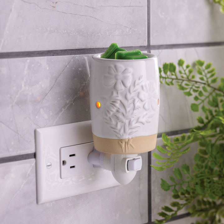 Garden Blooms botanical plug in wax melt warmer in a wall outlet beside green foliage