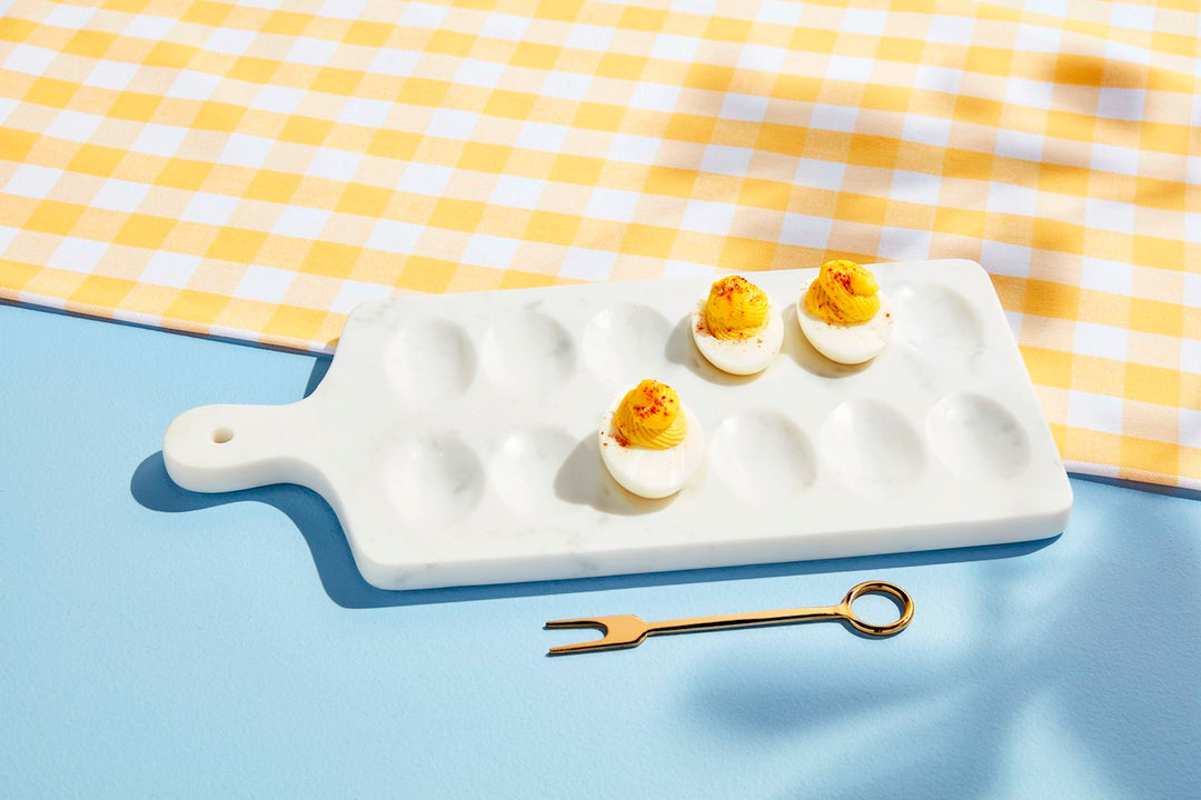 Deviled eggs on a white ceramic cutting board with a yellow and white checkered cloth in the background.