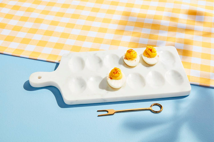 Deviled eggs on a white ceramic cutting board with a yellow and white checkered cloth in the background.