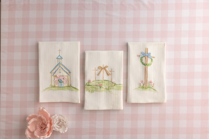 Three embroidered pictures of a church, cross, and wreath on a pink checkered background.