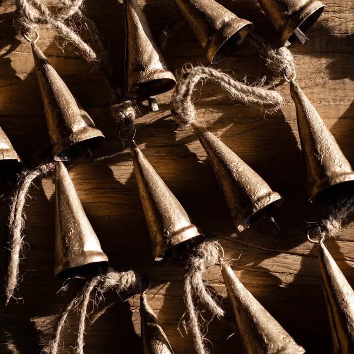 Vintage-style tapered bronze iron bell ornaments with rustic hanging loops arranged on a wood surface.
