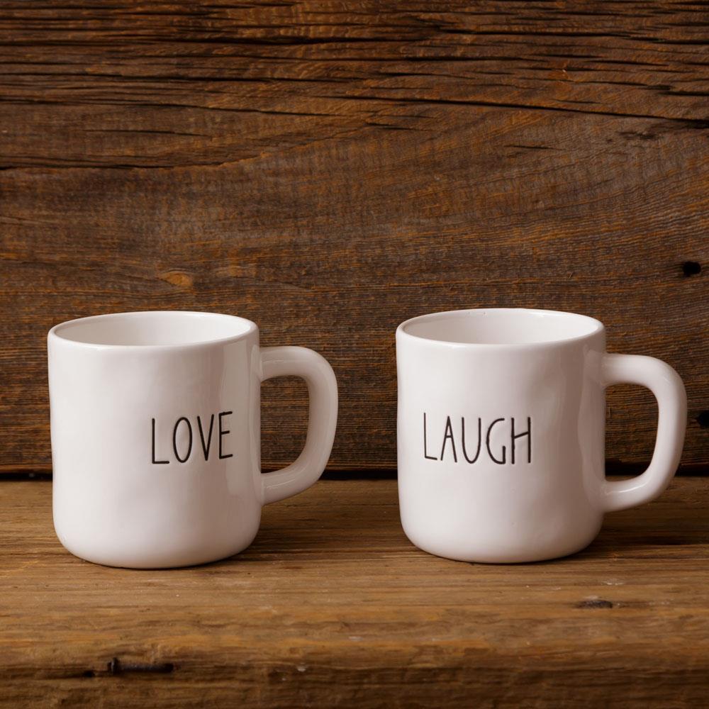 Two white mugs with 'LOVE' and 'LAUGH' text on a wooden surface and background.