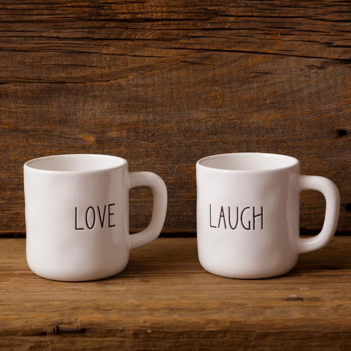 Two white mugs with 'LOVE' and 'LAUGH' text on a wooden surface and background.