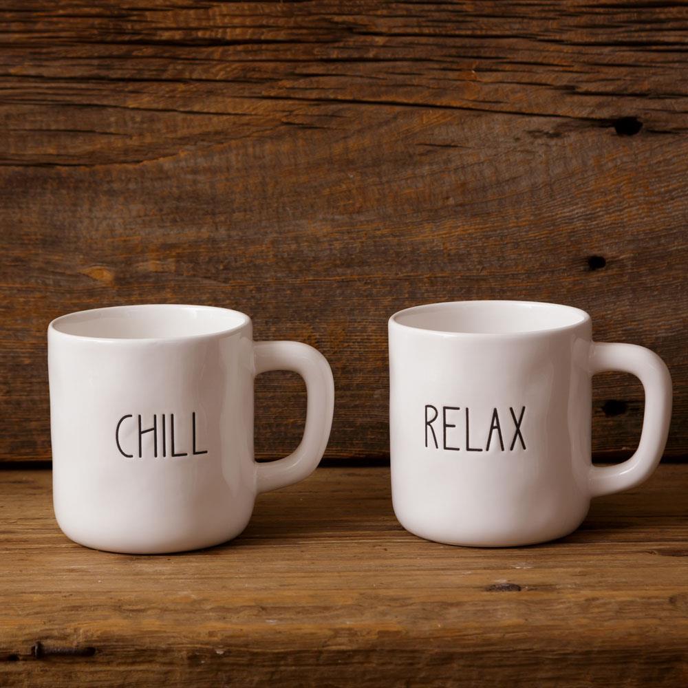 Two white mugs with 'CHILL' and 'RELAX' text on a wooden surface and background.