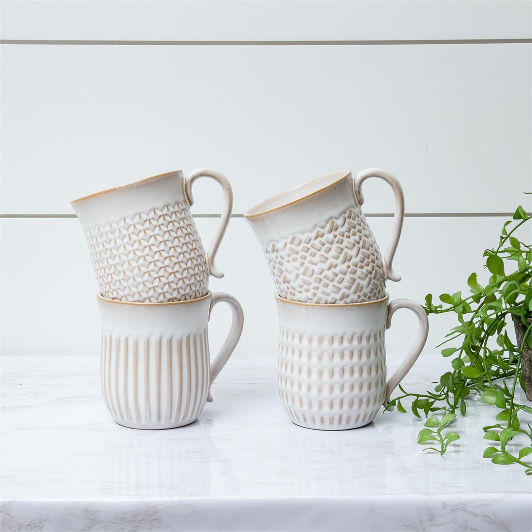 Set of white ceramic mugs with textured designs on a light surface with a plant in the background.
