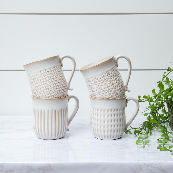 Set of white ceramic mugs with textured designs on a light surface with a plant in the background.