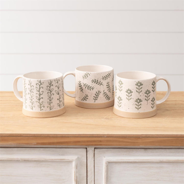 Three ceramic mugs with floral patterns on a wooden surface.