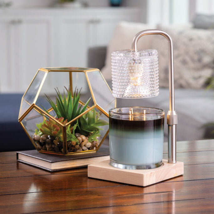 Decorative candle holder with succulent plant, glass candle, and lamp on a wooden table.