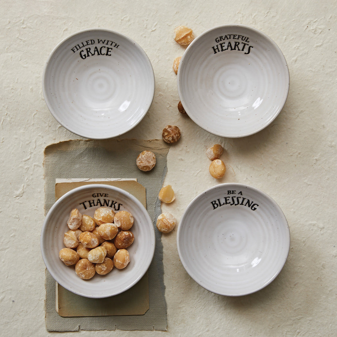 Four white bowls with text on a textured surface with small round objects.