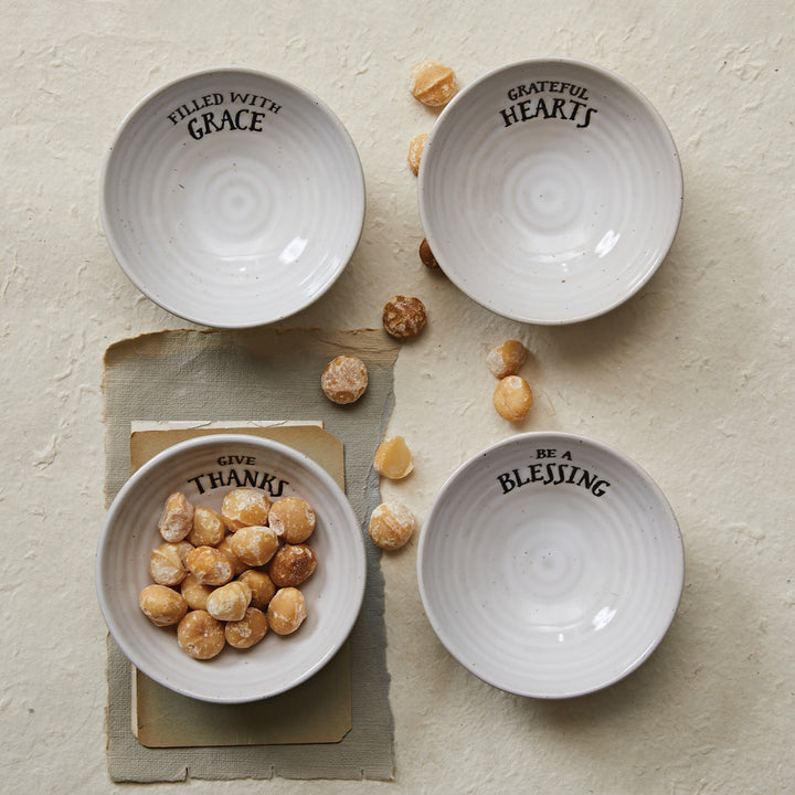 Four white bowls with text on a textured surface with small round objects.