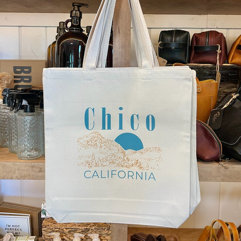 Tote bag with 'Chico California' text hanging on a rack with shoes in the background