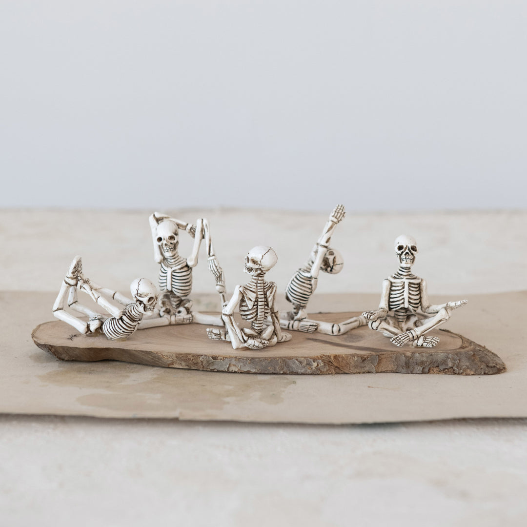 Set of silver skeleton figurines in various poses on a wooden board with a plain background