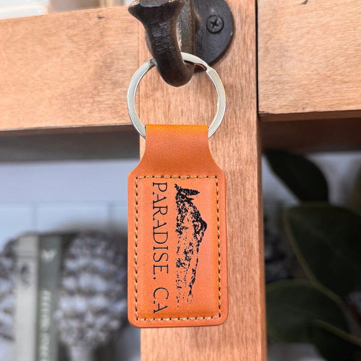 Brown leather keychain with 'Paradise, CA' engraving on a wooden surface.