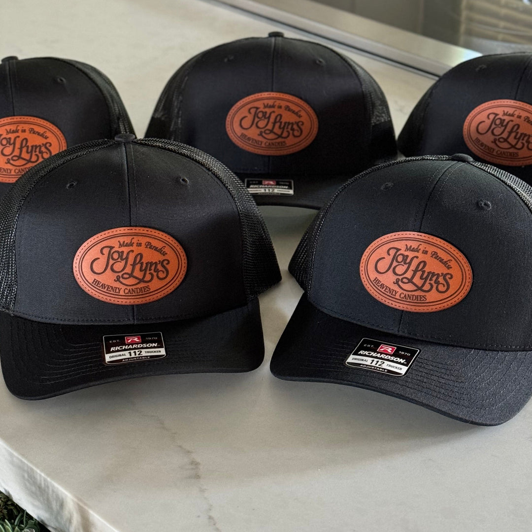 Five black baseball caps with leather patches on a marble countertop.