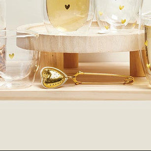 Tea-making setup with glass jars, cups, and a jar labeled 'loose tea' on a white surface.