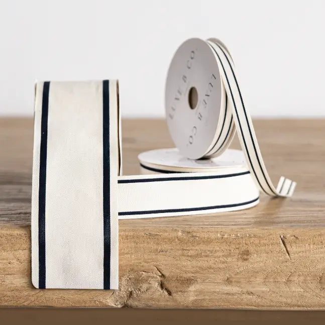 Close-up of wide cream woven ribbon with black border trim on a wood surface.