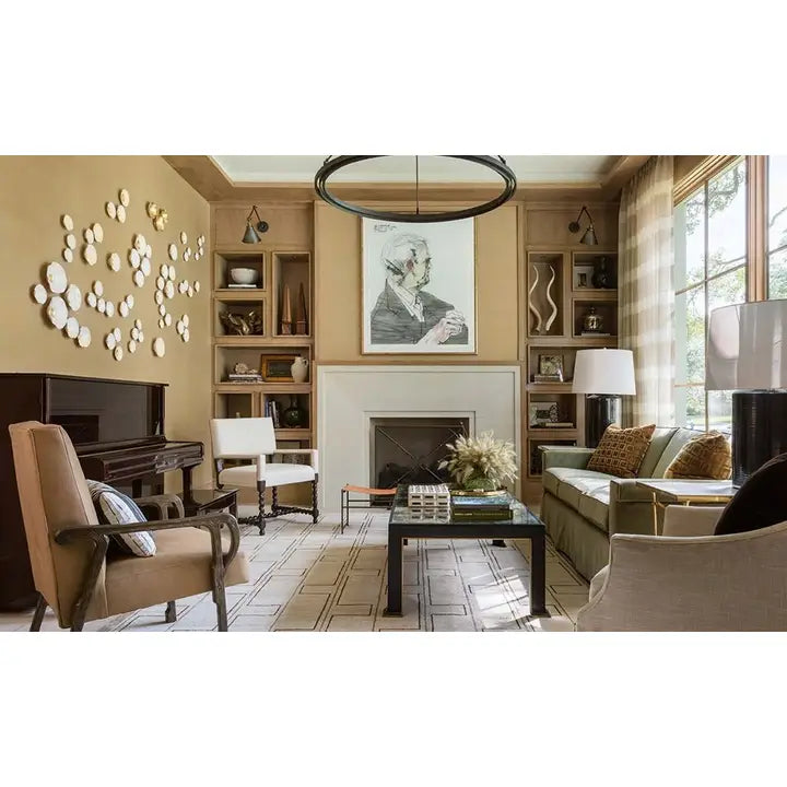 A styled living room interior with beige walls, built-in wood shelving, a fireplace, a large framed portrait, a black coffee table, upholstered seating, and decorative wall art.