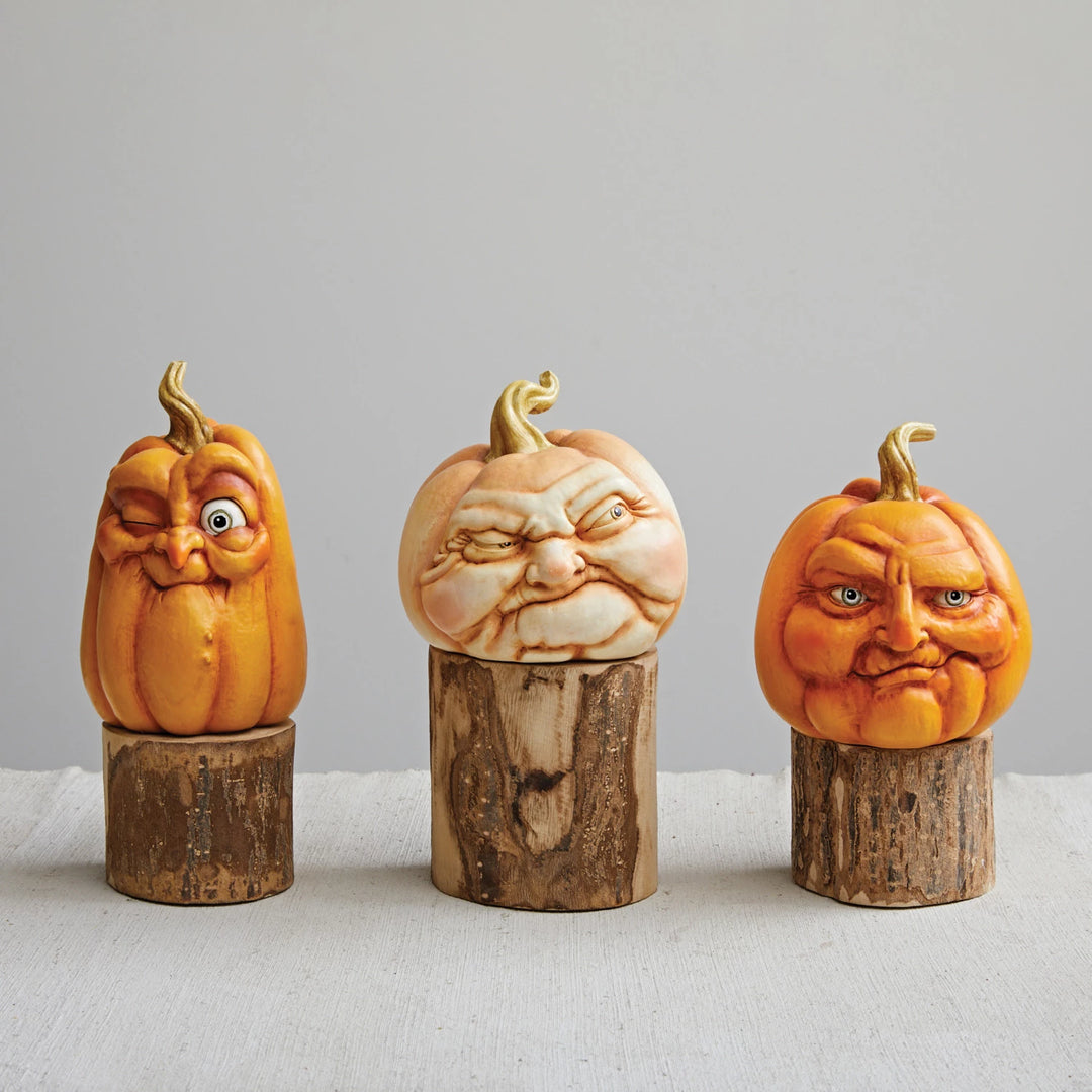 Three pumpkin carvings with facial expressions on wooden stands against a gray background