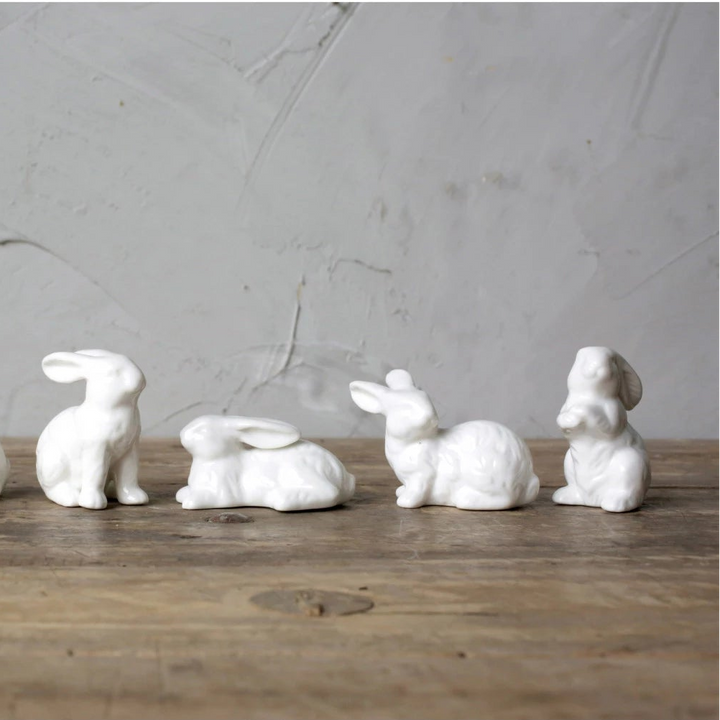 Four white ceramic rabbit figurines on a wooden surface with a gray concrete wall background.