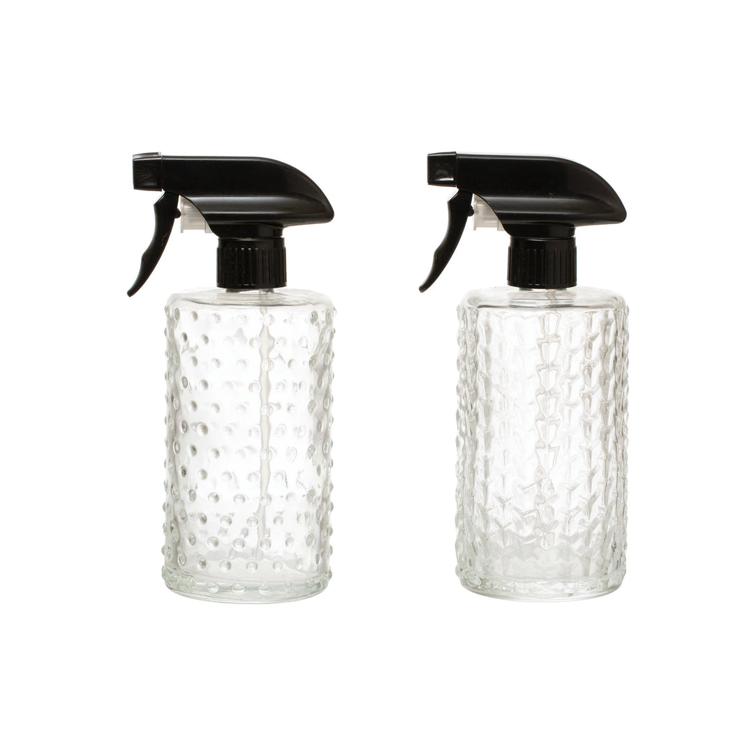 Two clear glass spray bottles with black nozzles on a white background