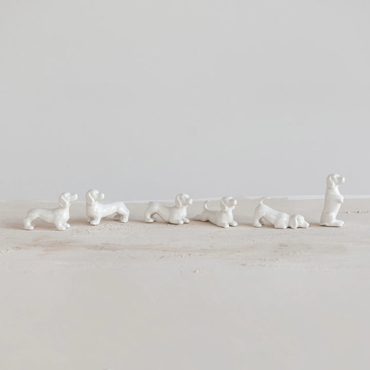 Set of white ceramic dog figurines on a light wooden surface with a white background