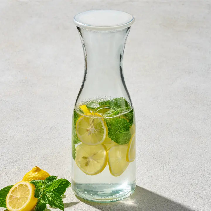 Clear 1-liter glass carafe with lid filled with lemon slices, mint, and water on a light surface.