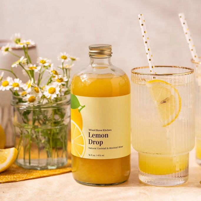 Bottle of Lemon Drop juice with two glasses and lemons on a table.