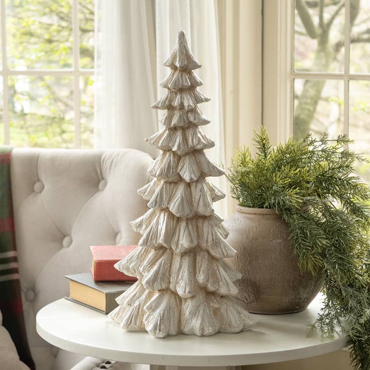 Cream tabletop Christmas tree with layered sculpted branches and a glittered finish, displayed beside greenery