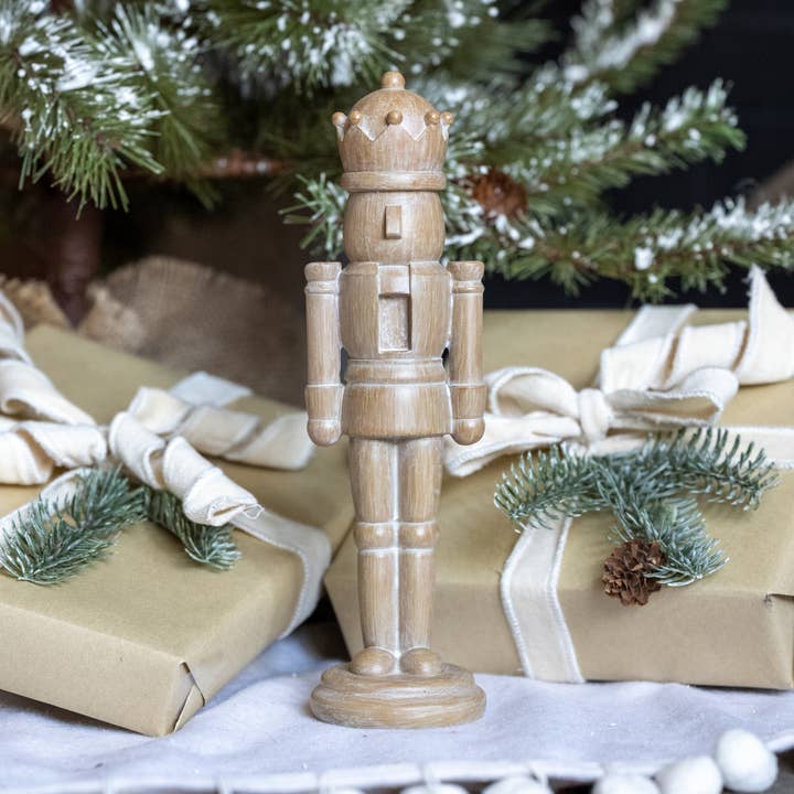 Neutral wood-look tabletop nutcracker with gold-toned crown accents, styled with Christmas greenery and ivory ribbon