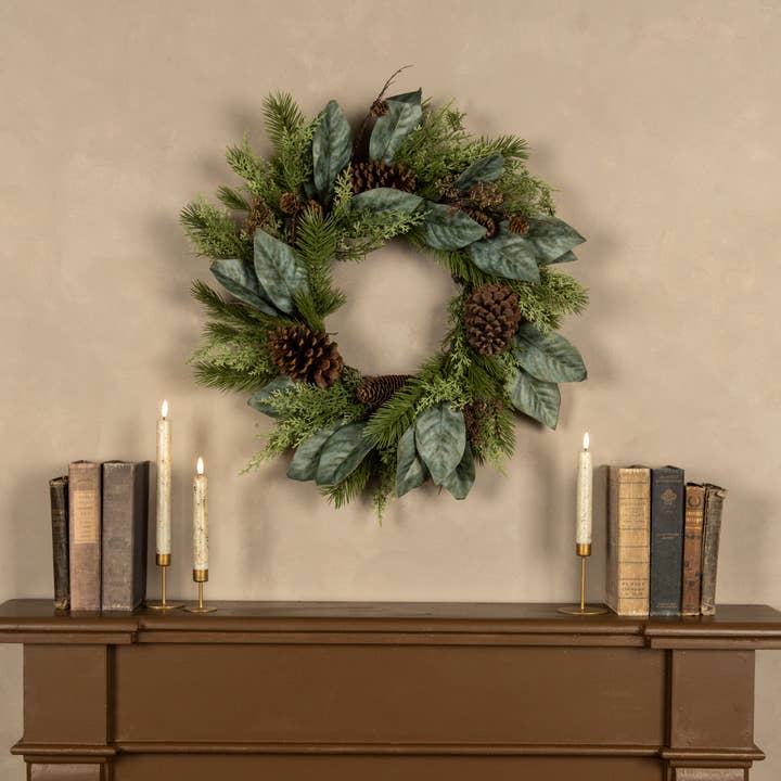 Green cedar, pine and magnolia wreath with broad leaves and brown pinecones on a neutral wall
