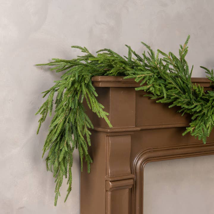 Soft touch Norfolk pine garland with green cascading branches draped across a mantel