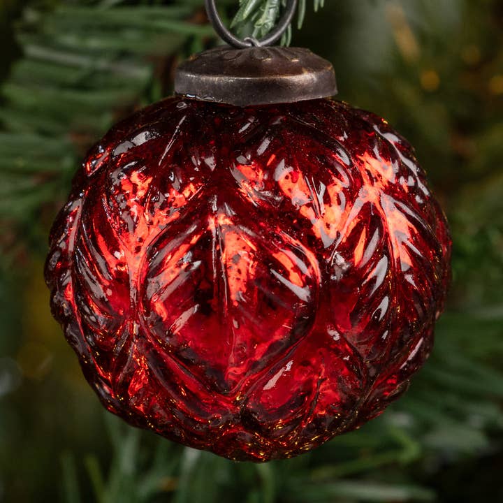 Reflective red ball Christmas ornament with a textured leaf pattern and dark hanging cap on evergreen foliage
