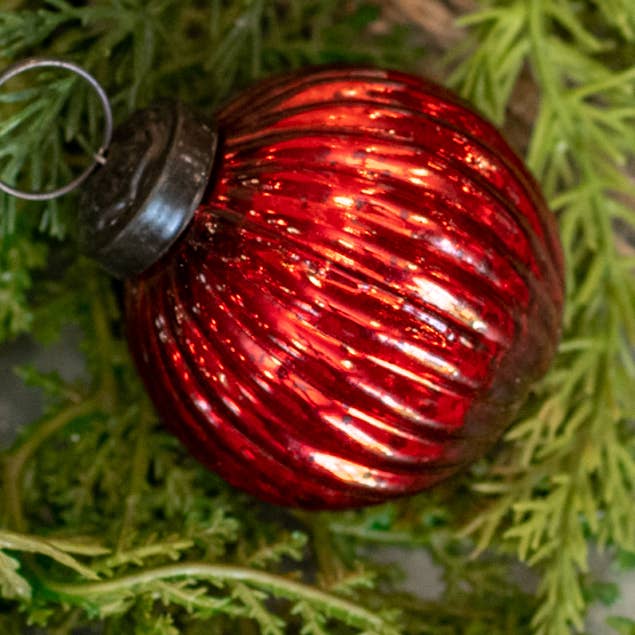 Red glass ball Christmas ornament with diagonal spiral ribbing, an aged-looking finish, and a dark hanging cap