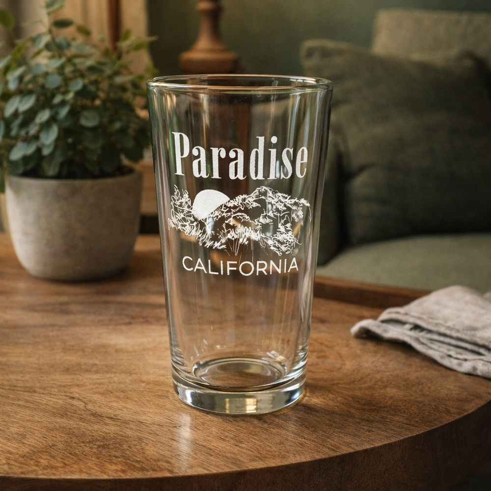 Clear glass with 'Paradise California' text on a wooden table in a cozy room.