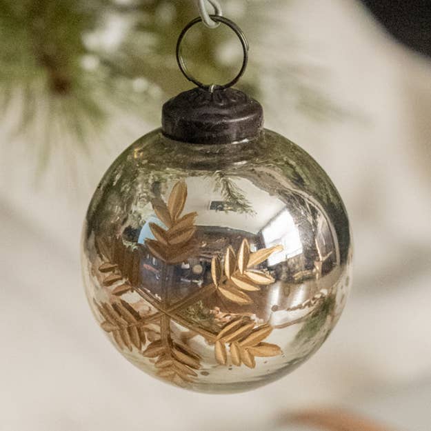 Reflective silver Christmas ball ornament with a gold-colored snowflake design, dark cap, and hanging loop