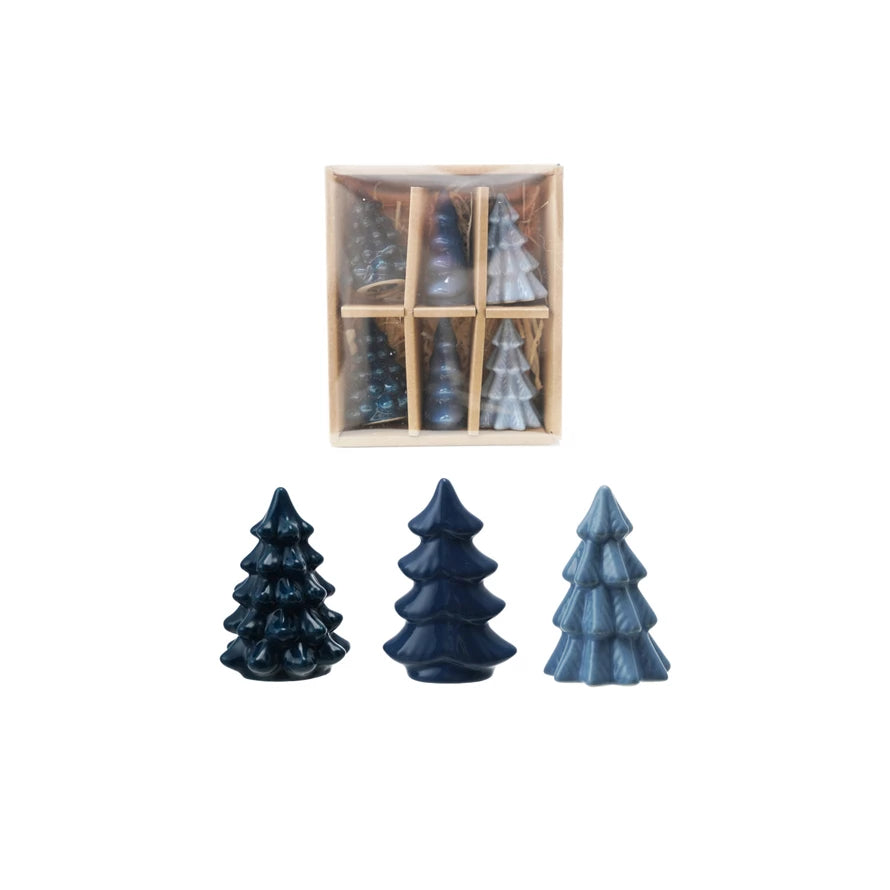 Set of three blue ceramic Christmas tree-shaped candles in front of a wooden box containing more candles.